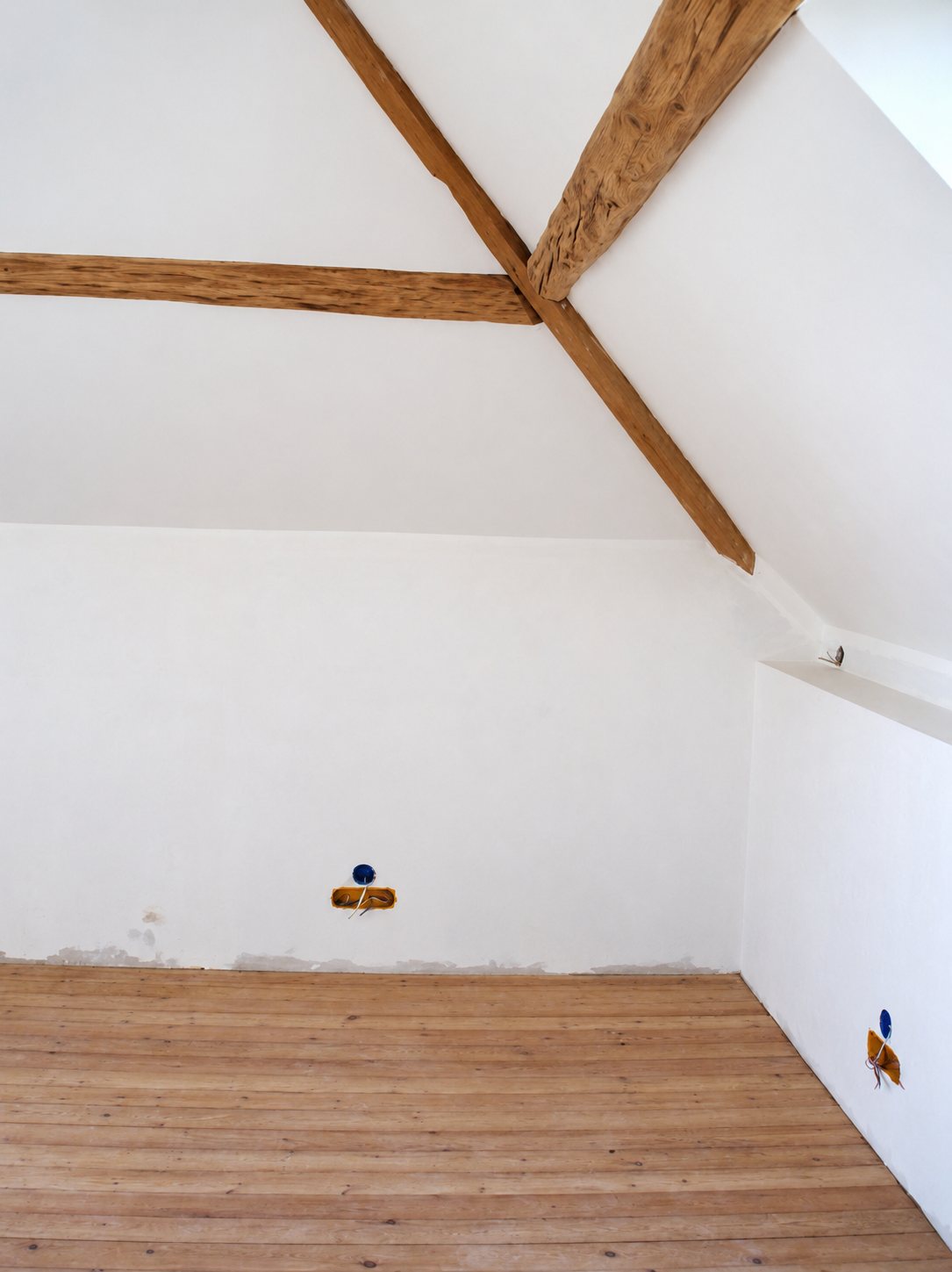 Pièce sous les combles aux murs blancs fraîchement enduits, avec poutres en bois apparentes et parquet clair non fini.