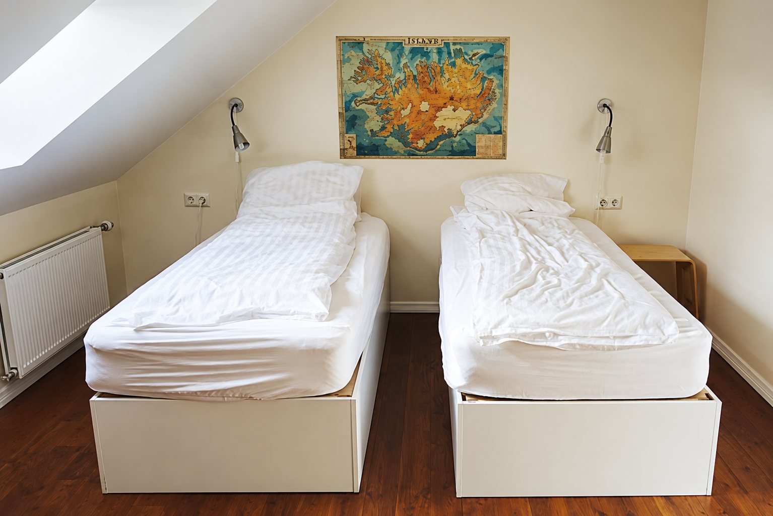 Chambre sous les combles avec deux lits simples aux draps blancs, des lampes murales et une carte de l'Islande accrochée au mur.
