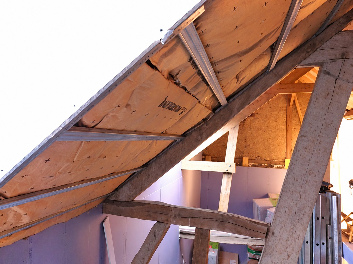 Vue de l'intérieur d'un comble avec une charpente traditionnelle en bois et des panneaux d'isolation fixés sous le rampant du toit.