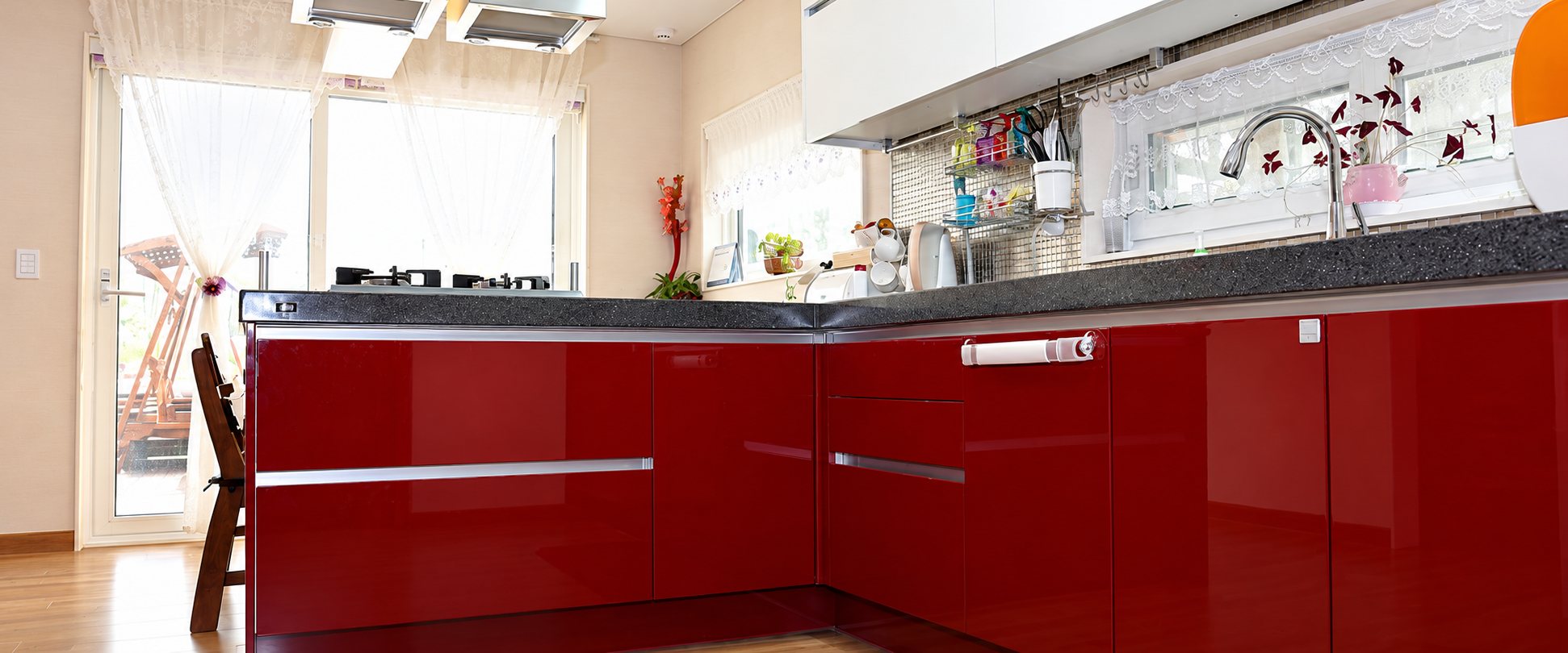 Une cuisine lumineuse équipée de meubles bas rouge brillant, d'un plan de travail en granit gris foncé et d'une grande baie vitrée.