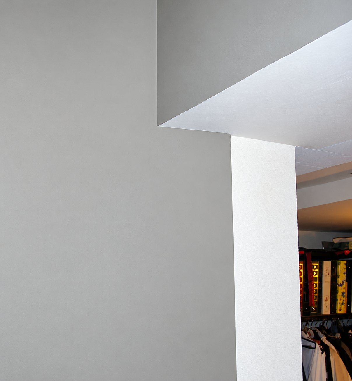 Un mur peint en gris clair et un angle de plafond blanc, avec une penderie de vêtements visible à droite.