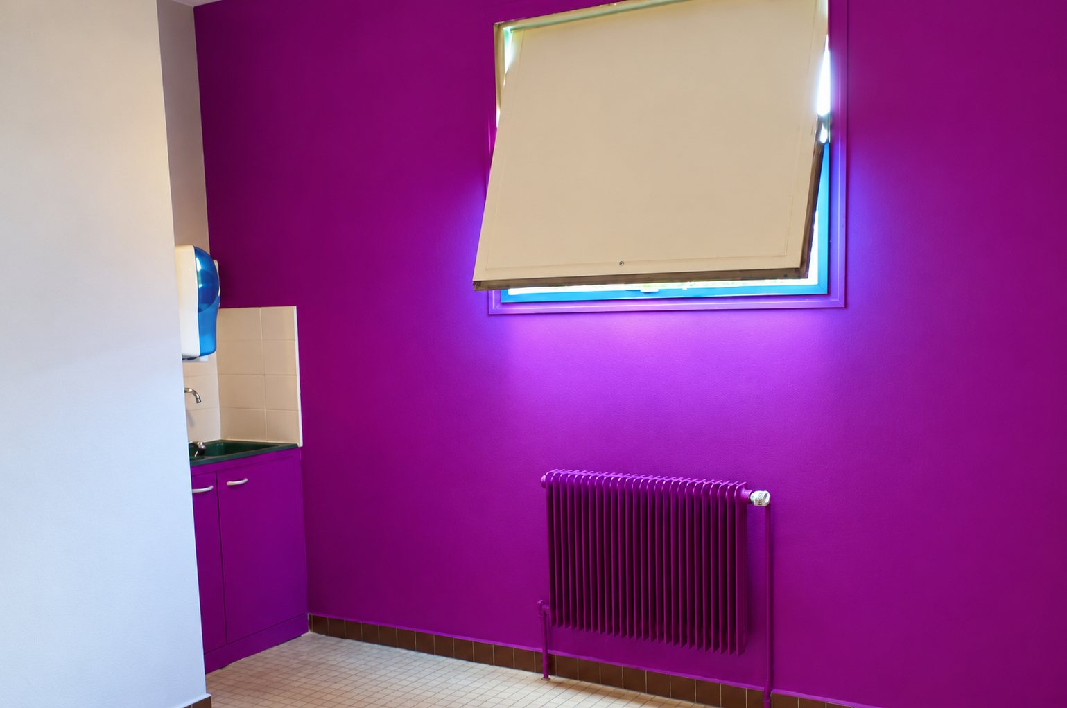 Pièce repeinte en violet vif avec un radiateur assorti, une fenêtre entrouverte éclairée de néons bleus et un petit meuble d'évier à gauche.