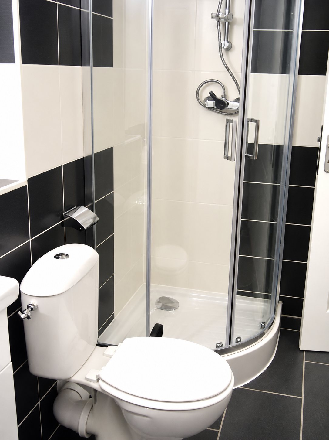 Petite salle de bain rénovée avec carrelage noir et blanc, une cabine de douche d'angle en verre et un WC blanc au premier plan.